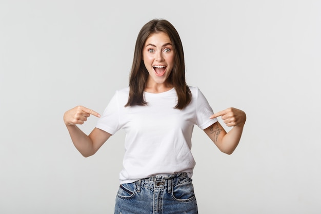 Excité fille brune heureuse souriant, pointant du doigt le logo