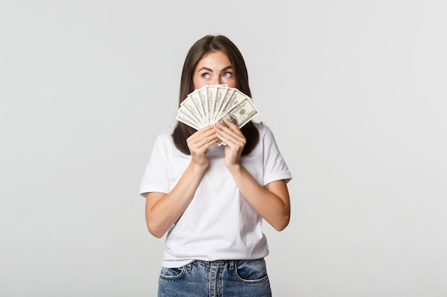 Excité fille rêveuse tenant de l'argent et regardant le coin supérieur gauche, pensant au blanc.