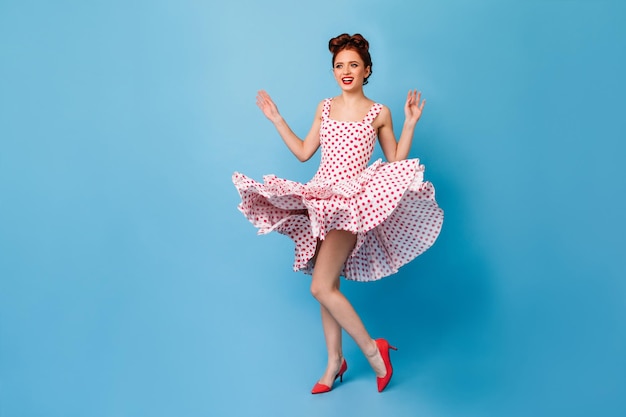 Excité fit femme en tenue de pin-up dansant sur fond bleu Studio shot of smiling ginger girl in polkadot dress