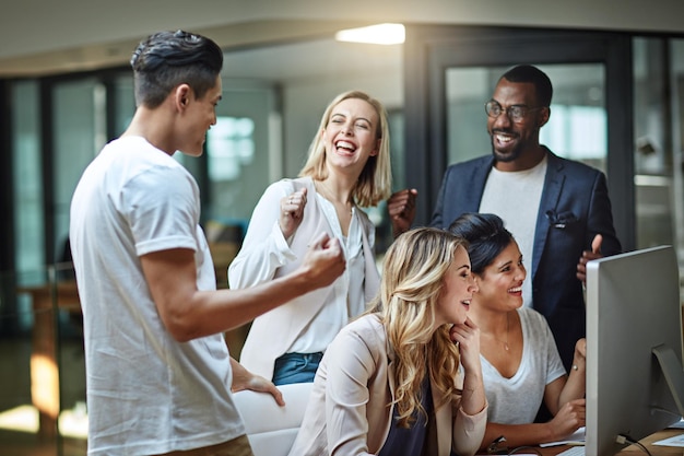 Excité heureux et célébrant les agents de marketing applaudissant après avoir atteint l'objectif et la date limite au bureau tard dans la nuit Équipe créative diversifiée avec un geste de la main du poing réussi tout en travaillant sur un ordinateur