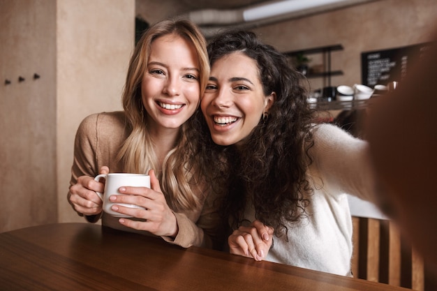 excité heureux jolies filles amis assis dans un café prendre un selfie par caméra