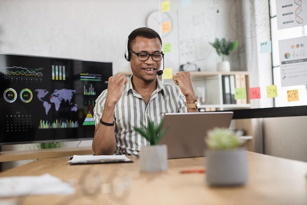 Excité hurlant jeune homme d'affaires afro-américain ou entrepreneur travaillant avec un ordinateur portable