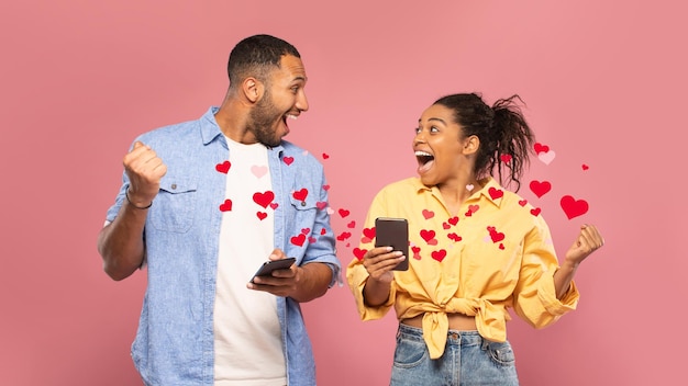 Photo excité jeune couple noir à l'aide de téléphones portables et de gestes