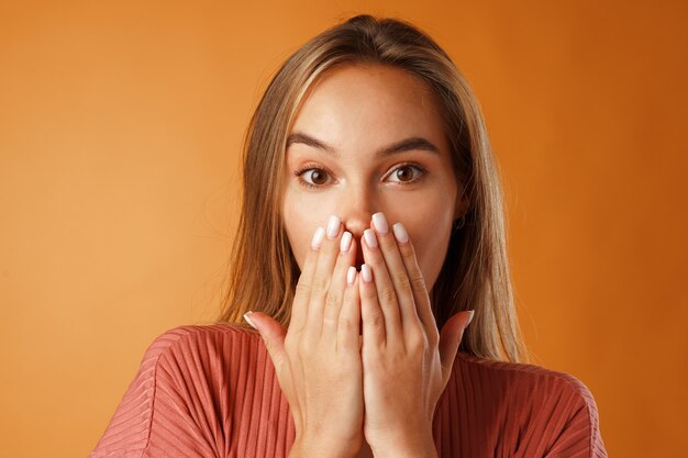 Excité jeune femme fermant la bouche avec sa main sur fond orange