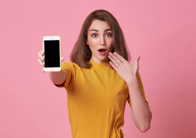 excité jeune femme montrant au téléphone mobile écran blanc isolé sur fond rose