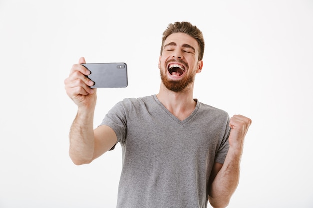 Excité jeune homme jouer à des jeux par téléphone portable faire un geste gagnant.