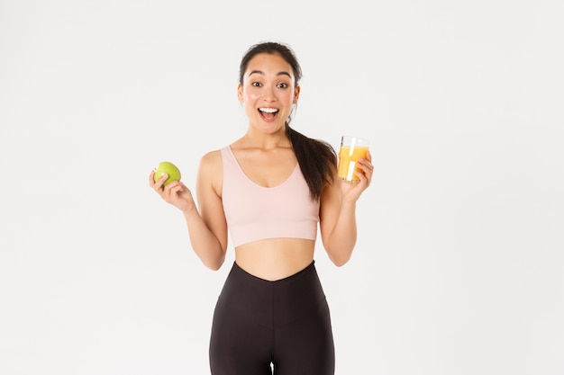 Excité jolie fille asiatique de remise en forme, sportive avec pomme et jus d'orange haletant étonné et heureux, manger sainement pour rester en forme