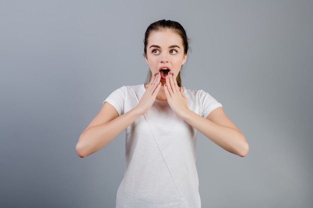 Excité surprise fille brune couvrant sa bouche avec les mains isolées sur gris