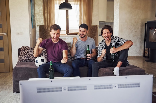 Excité trois amis regardant le football à la télévision à la maison ensemble.