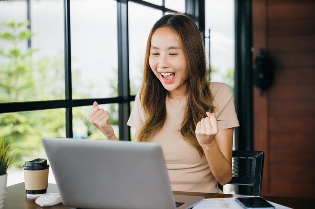 Excitée heureuse jeune femme d'affaires asiatique assise avec un ordinateur portable