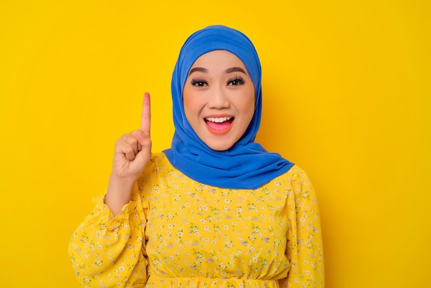 Excitée jeune belle femme musulmane asiatique levant le doigt vers le haut ayant une idée isolée sur fond jaune