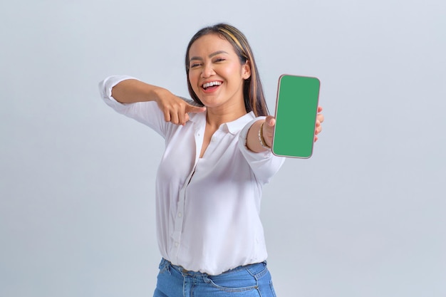 Excitée jeune femme asiatique montrant un téléphone mobile à écran vide recommandant une application mobile isolée sur fond blanc
