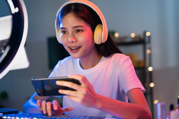 Excitée jeune femme asiatique portant un casque et jouant à un jeu en ligne sur smartphone avec diffusion en direct sur internet