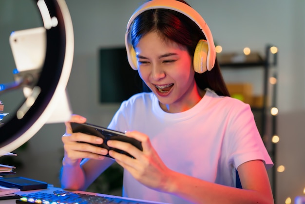 Excitée jeune femme asiatique portant un casque et jouant à un jeu en ligne sur smartphone avec diffusion en direct sur internet.