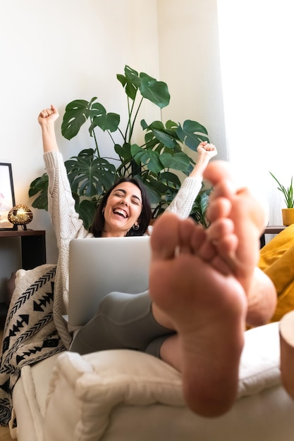 Excitée jeune femme caucasienne levant les bras pour célébrer le succès ou la réussite à la maison à l'aide d'un ordinateur portable Espace de copie Image verticale Concept de victoire