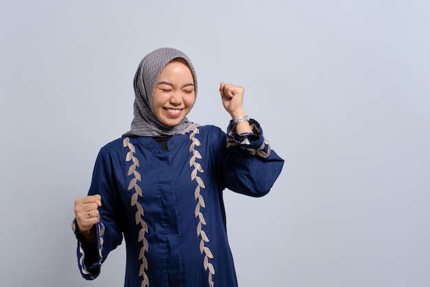 Excitée jeune femme musulmane asiatique levant le poing vers le haut célébrant le succès isolé sur fond blanc