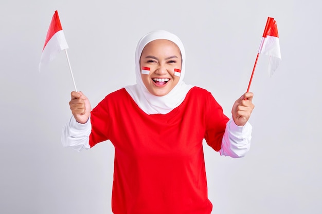 Excitée jeune femme musulmane asiatique en tshirt blanc rouge tenant le drapeau indonésien pour célébrer le jour de l'indépendance indonésienne le 17 août isolé sur fond blanc