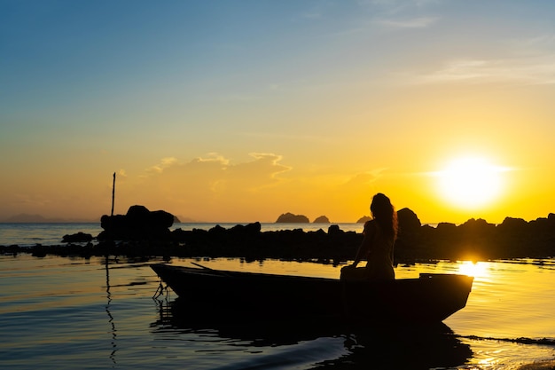 Excursion en bateau romantique avec une fille au coucher du soleil La fille est assise dans un bateau en bois sur l'océan