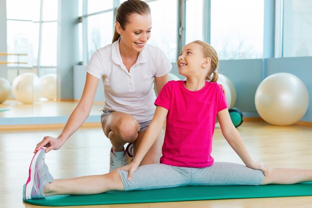 Exercice avec instructeur. Instructeur joyeux aidant une petite fille avec des exercices d'étirement dans un club de sport