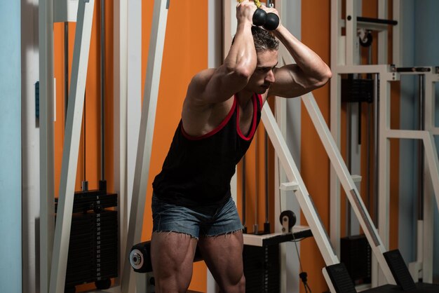 Exercice de jeune culturiste dans la salle de gym, il effectue des poussées de triceps à deux bras