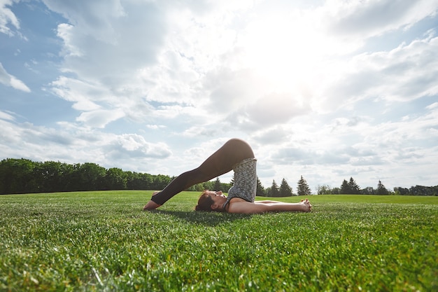 Exercices d'étirement jeune femme en vêtements de sport faisant du yoga à l'extérieur sur une herbe verte ensoleillée