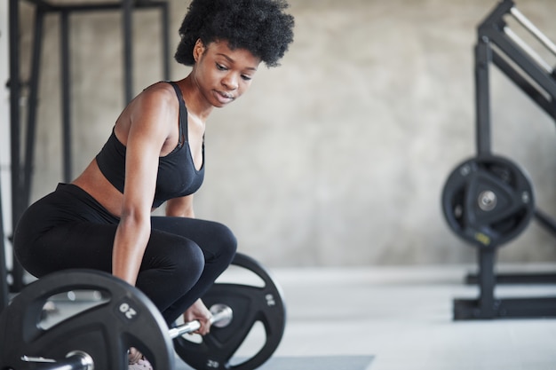 Exercices De Levage. Femme Afro-américaine Aux Cheveux Bouclés Et En Vêtements Sportifs Ont Une Journée De Remise En Forme Dans La Salle De Sport