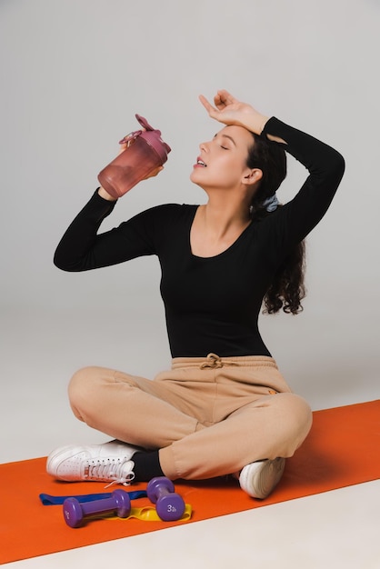 Exercices de modèle de forme physique avec des haltères et boit de l'eau d'une bouteille de sport