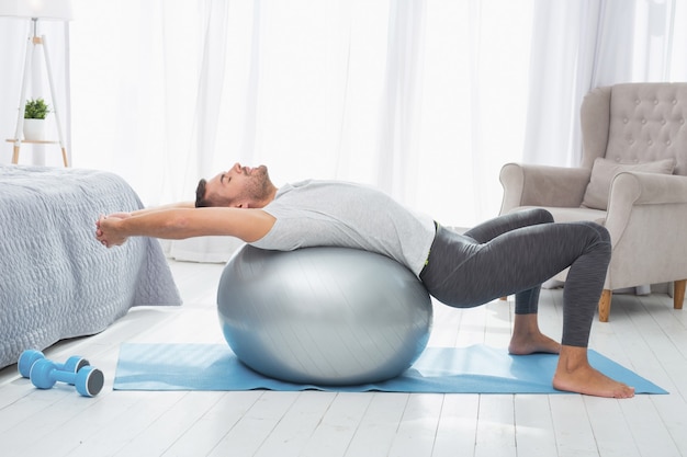 Exercices sportifs. Bel homme bien construit allongé sur un ballon médical pendant l'exercice