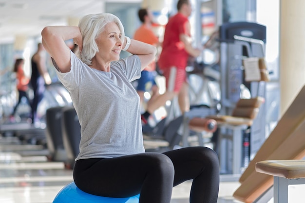 Exercices utiles. Femme senior assez saine en riant et en faisant de l'exercice alors qu'il était assis sur un ballon en forme.