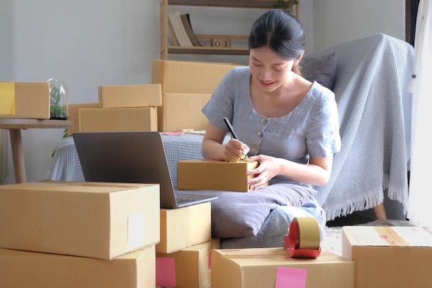 Expédition achats en ligne jeune démarrage propriétaire de petite entreprise écrivant l'adresse sur une boîte en carton sur le lieu de travailpetite entreprise entrepreneur PME ou femme asiatique indépendante travaillant avec une boîte à la maison