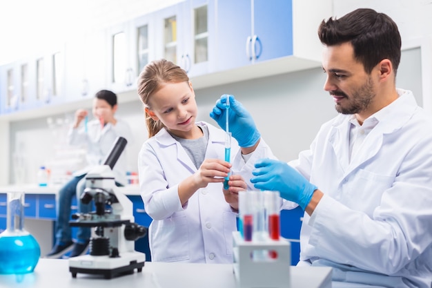 Expérimenter ensemble. Charmant bel homme aider la petite fille à effectuer un test tout en posant au laboratoire