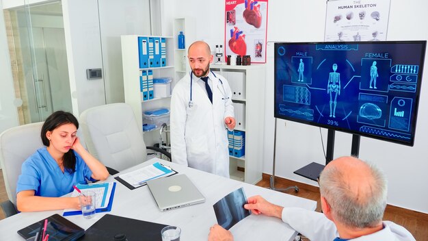 Expert médical parlant des soins de santé lors d'un séminaire avec le personnel hospitalier dans la salle de conférence pointant sur un moniteur numérique. Hérapiste de clinique discutant avec des collègues de la maladie, de la profession médicale