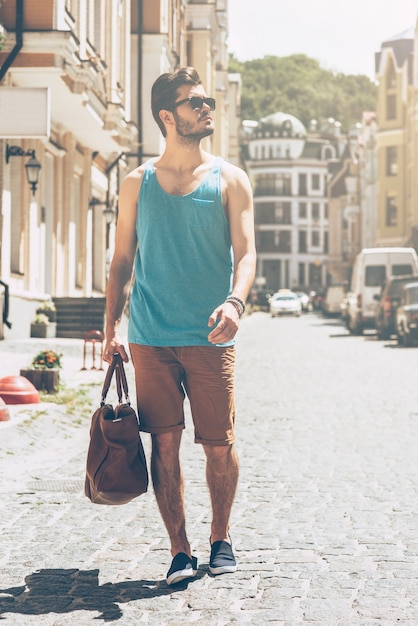 Explorer la ville. Toute la longueur du beau jeune homme dans un sac de transport de vêtements décontractés et en détournant les yeux en marchant le long de la rue