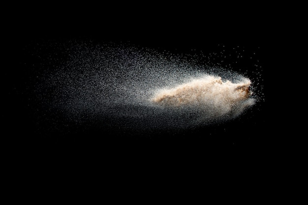 Explosion de sable isolée sur fond noir. Figer le mouvement des éclaboussures de poussière de sable.