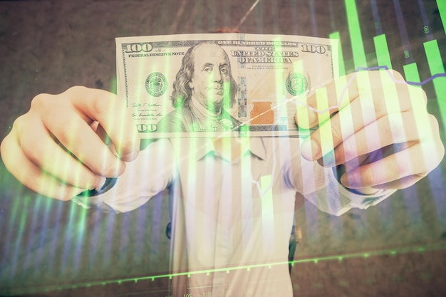 Exposition multiple du graphique forex dessinant l'hologramme et les billets en dollars américains et les mains de l'homme Concept d'analyse technique