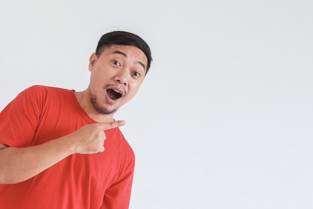 Expression du visage surpris d'un homme asiatique heureux en t-shirt rouge avec la main pointant sur un espace vide