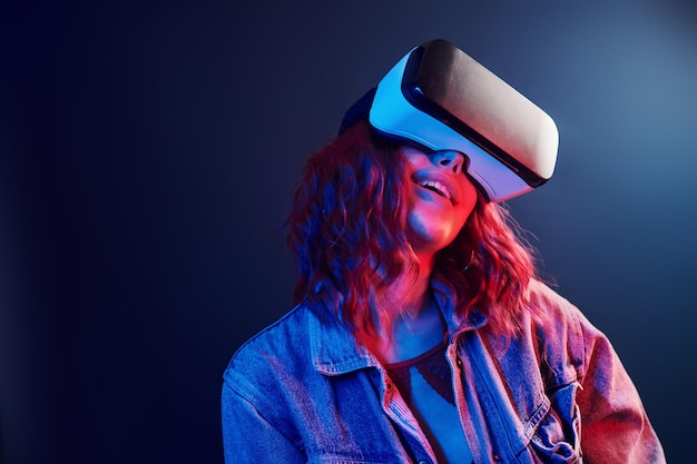 Expression faciale de jeune fille avec des lunettes de réalité virtuelle sur la tête en néon rouge et bleu en studio