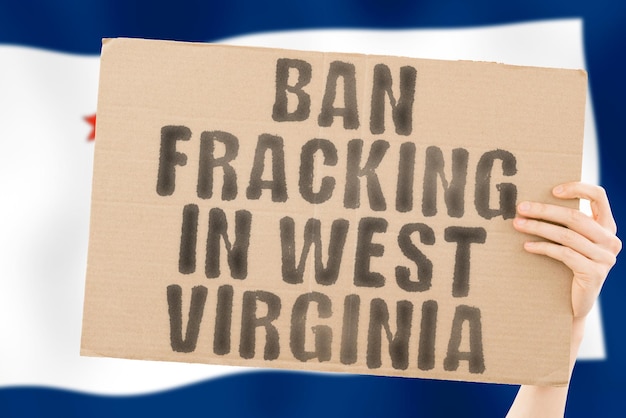 L'expression Interdire la fracturation hydraulique en Virginie-Occidentale sur une bannière dans la main des hommes avec le drapeau flou de la Virginie-Occidentale sur l'arrière-plan Extrait de la nature Stop Pipe Energy Drill Raw Power Fuel Fossil Crisis