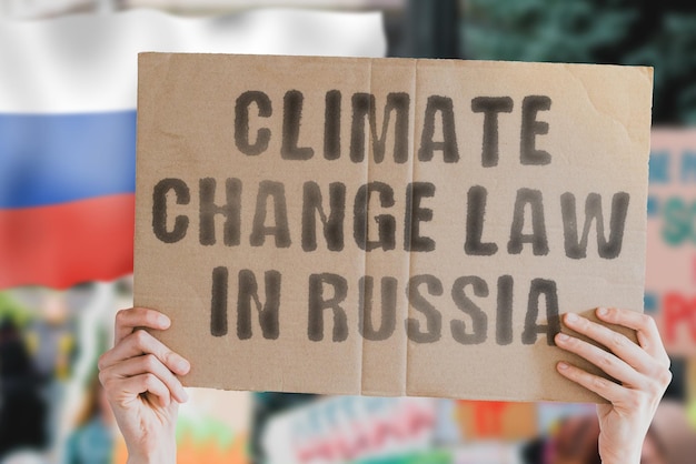 L'expression « loi sur le changement climatique en Russie » sur une bannière dans la main des hommes avec un drapeau russe flou en arrière-plan. Protection de l'environnement. La nature. Législation. Règles. Politique