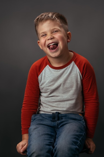 Expressions faciales émotions sentiments drôles garçon riant en chemise rouge avec les yeux fermés enfant heureux sur dar...