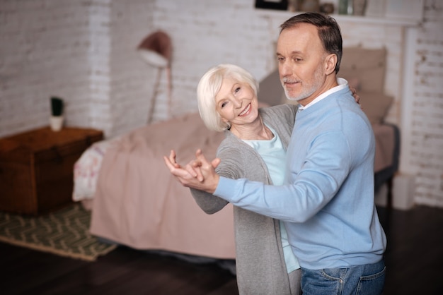 Exprimer son bonheur. Dame âgée souriante dansant avec son mari aimant à la maison.