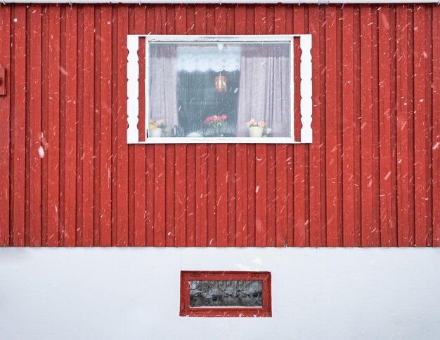 Extérieur du mur en bois dur rouge et du cadre de fenêtre de la maison nordique de pêche en hiver dans les îles Lofoten