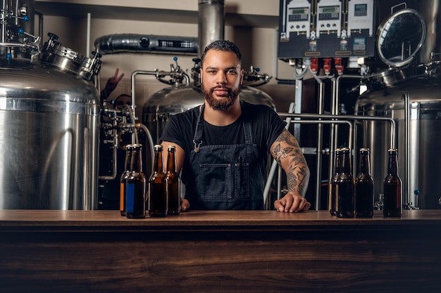 Fabricant masculin hipster tatoué à barbe noire présentant de la bière artisanale dans la microbrasserie.