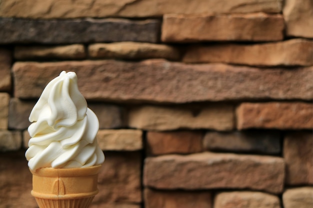 Façade, cornet de crème glacée au service doux au lait blanc vanillé blanc avec mur de blocs de pierre brun foncé flou en arrière-plan