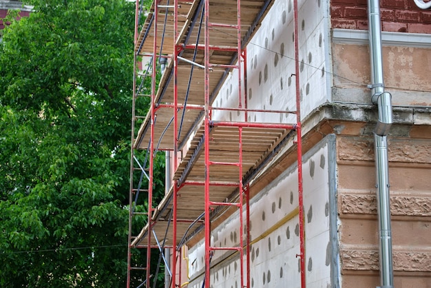 Façade du bâtiment en cours de rénovation avec cadre d'échafaudage de construction Isolation des murs avec des feuilles de polystyrène pour une maison éconergétique