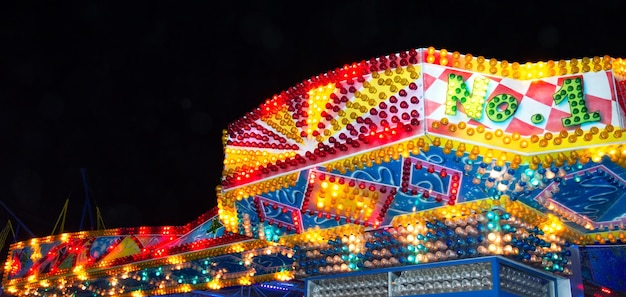 Une façade lumineuse d'ampoules multicolores éclatantes sur fond de ciel nocturne. Gros plan, bannière. Parc d'attractions, foire.