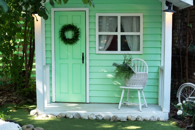 Façade maison en bois verte décorée pour les vacances et véranda cosy avec chaise et panier fleurs