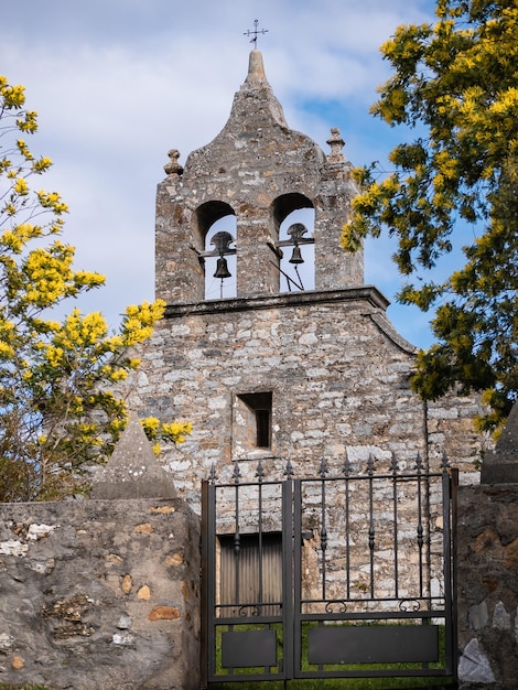 Façade principale de l'Ermitage de la Virgen de la Estrella située dans la ville de San Juan de Paluezas à El Bierzo Clocher de l'église entouré de fleurs jaunes et d'une croix au sommet derrière une porte métallique