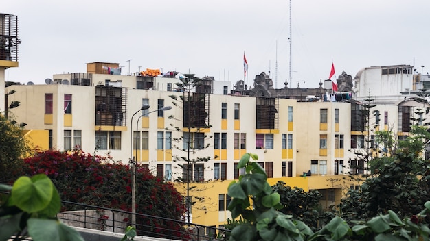 Façade vieillie d'un immeuble résidentiel de couleur moderne à plusieurs étages dans le centre historique de Lima au Pérou, murs jaunes et oranges, arbres.