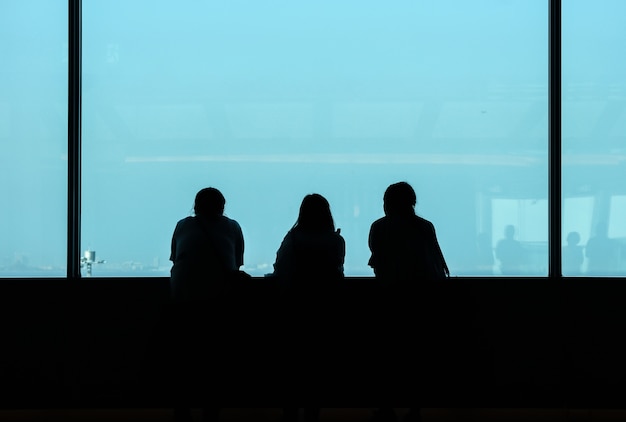 Face arrière de trois femmes qui regardent la ville depuis la haute fenêtre du bâtiment.